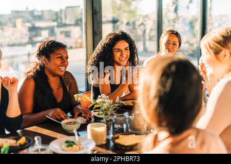 Happy female friends sitting and having breakfast together at retreat center Stock Photo