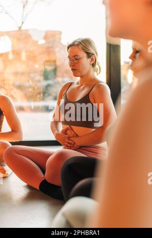 Woman with hands on stomach sitting cross-legged at retreat center Stock Photo