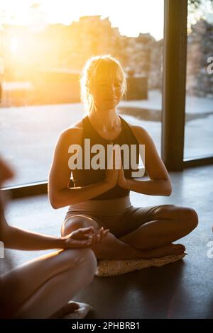 Woman with hands clasped practicing prayer pose while meditating at retreat center Stock Photo