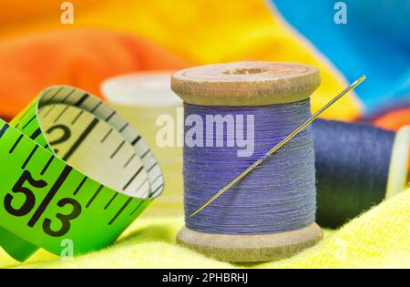 Sewing item tools isolated on colored clothing with macro details including spools of thread, needle, and tape measure. Stock Photo