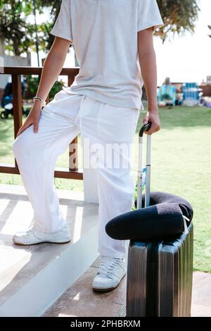 Low section of teenage boy with suitcase and neck pillow at villa during vacation Stock Photo