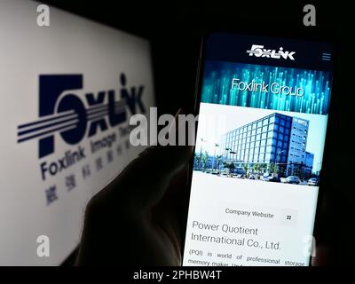 Person holding smartphone with webpage of company Foxlink Image Technology Co. Ltd. on screen in front of logo. Focus on center of phone display. Stock Photo