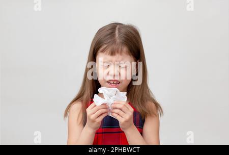 Child going to sneeze into napkin in hands showing allergic rhinitis or cold, caucasian little girl of 6 7 years on white background with closed eyes Stock Photo