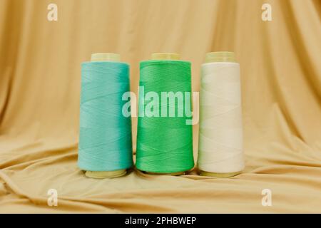 A close-up image of four colorful spools of thread, each with a different color, arranged on a plain fabric background Stock Photo
