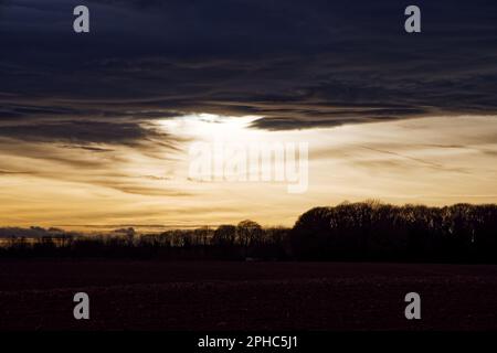 Winter sunset with dark clouds over ploughed fields with woodland on the horizon in the Doncaster countryside, South Yorkshire, England. Stock Photo
