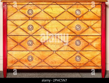 Vintage chest of drawers in bright orange with symmetrical patterns and brass handles. Stock Photo