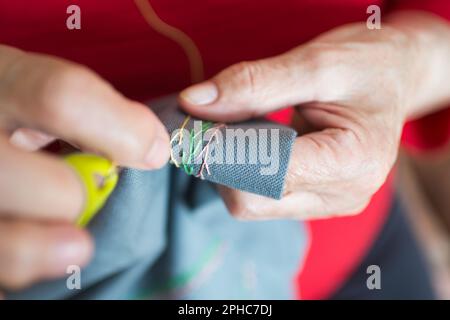 Close up of senior woman hands sewing at home. Yellow thumble Stock Photo