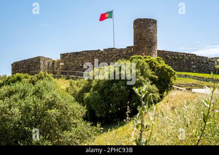 Idyllic low-angle view of castle Castelo de Aljezur with its tower and walls surrounded by green grass and bushes, featuring a waving Portuguese flag. Stock Photo