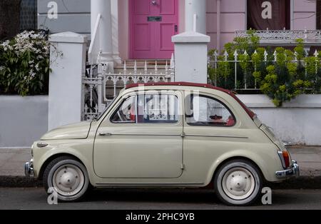 Cute beige coloured vintage Fiat 500 classic car parked in front of a house with a pink door on a residential street in Notting Hill, west London UK. Stock Photo