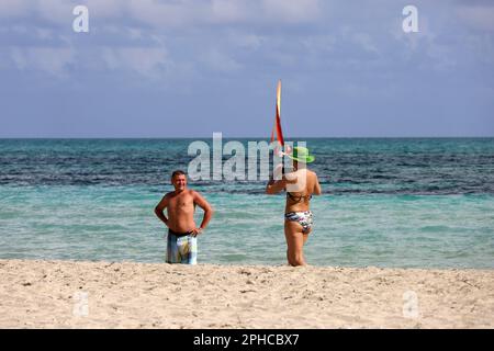 Woman photographing a man by smartphone on tropical sandy beach. Photo shooting by ocean coast, vacation and travel Stock Photo