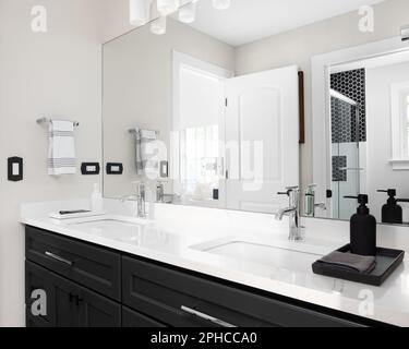 A bathroom with a black cabinet, white marble countertop with two sinks, and a view of the shower in the reflection. Stock Photo