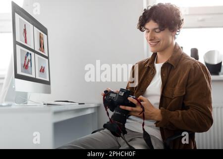 Photographer looking at photos on his DSLR camera, sitting at table with computer, man working with editing software Stock Photo
