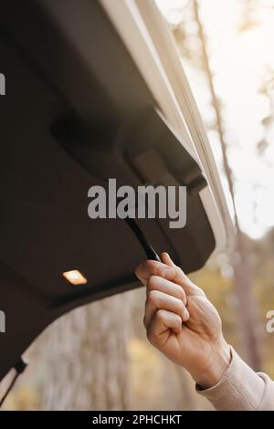 Unrecognisable man holds trunk handle and closes car trunk door outdoors in park. Interior details of prestige modern vehicle. Stock Photo