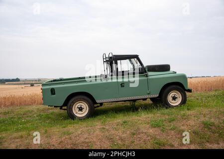 Land Rover Series Three pickup truck with soft top cab parked on grass in front of a barley field Stock Photo