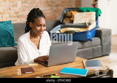 Positive black woman planning vacation travel with laptop, booking tickets or hotel room on web, free space Stock Photo