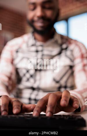 Selective focus on freelancer hands typing text while chatting using computer keyboard from home living room. Closeup of african american student writing homework while studying remote. Stock Photo