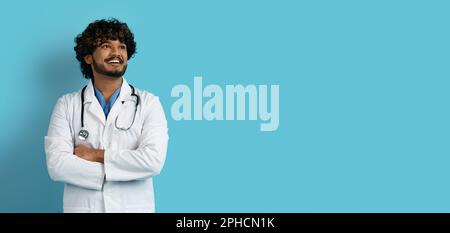 Happy young eastern doctor looking at copy space on blue Stock Photo