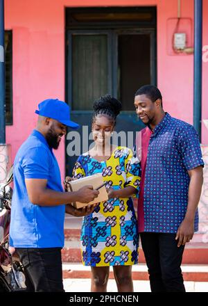 Happy Young Black African Couple receive cardboard boxes with products purchased online from delivery man, through local postal shipping and delivery Stock Photo