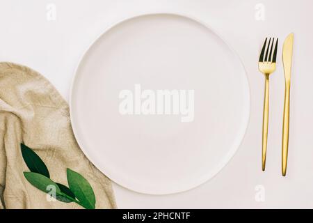 Empty plate and golden cutlery on the white table. Minimalist table setting, top view Stock Photo