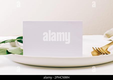 Blank paper card on the plate with golden cutlery close-up. Place card, invitation mock-up Stock Photo