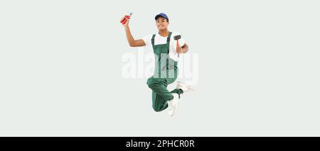 Jumping African-American young man in uniform and with tools on light background Stock Photo