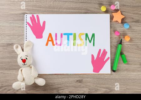 Flat lay composition of notebook with word Autism and toys on wooden table Stock Photo