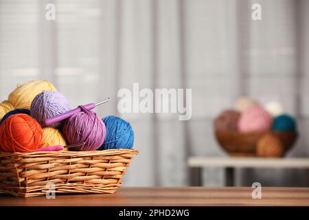 Wicker basket with clews of colorful knitting threads and crochet hooks on wooden table indoors. Space for text Stock Photo