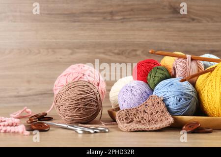 Clews of colorful knitting threads, crochet hooks, scissors and buttons on wooden table Stock Photo