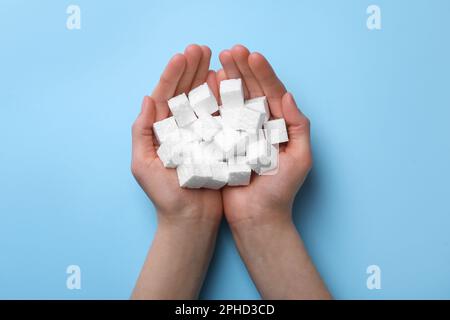 Woman with handful of styrofoam cubes on light blue background, top view Stock Photo