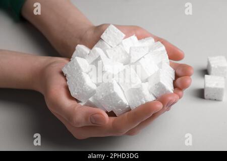 Woman with handful of styrofoam cubes on light grey background, closeup Stock Photo