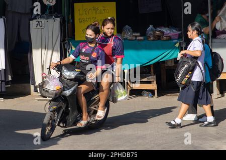 SAMUT PRAKAN, THAILAND, FEB 13 2023, Two women in aprons ride through the marketplace on a motorcycle Stock Photo