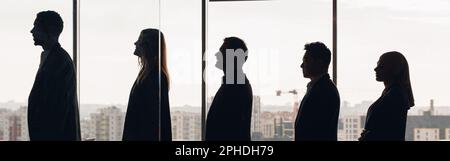 Silhouette photo of a group of businessmen standing side by side in profile in office Stock Photo
