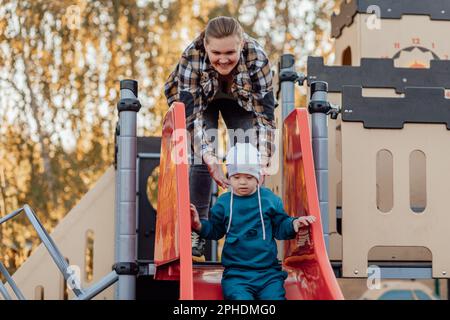 A boy, person with down syndrome walks in the park with his mother, going down the children's slide Stock Photo