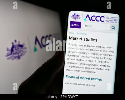 Person holding smartphone with website of Australian Competition and Consumer Commission on screen with logo. Focus on center of phone display. Stock Photo