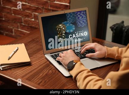 Man playing poker on laptop at wooden table, closeup. Casino online Stock Photo