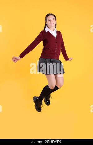 Teenage girl in school uniform jumping on yellow background Stock Photo