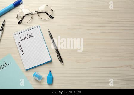 Flat lay composition with unfilled To Do list in notepad and pens on wooden table, space for text Stock Photo