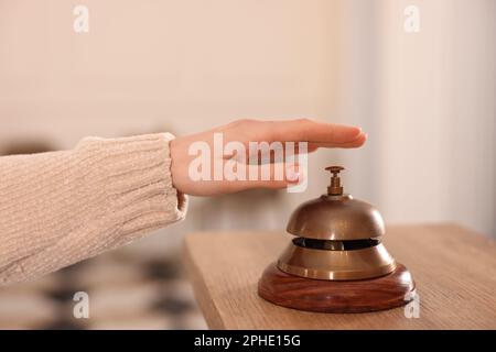 Woman ringing hotel service bell at wooden reception desk, closeup Stock Photo