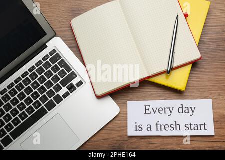 Note with motivational quote Every day is a fresh start, modern laptop and office stationery on wooden table, flat lay Stock Photo