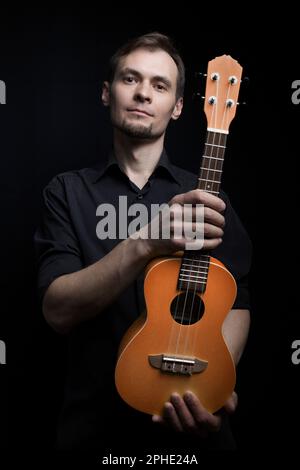Handsome young low key man portrait with ukulele guitar over black background Stock Photo
