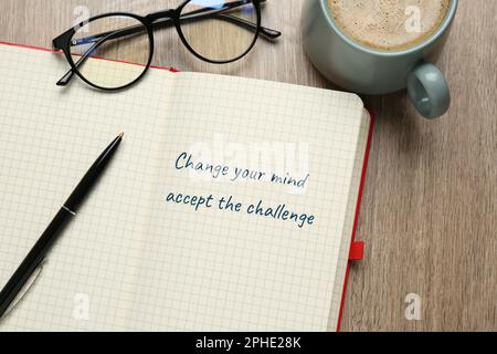 Motivational quote Change Your Mind Accept The Challenge written in notebook, eyeglasses and cup of coffee on wooden table, flat lay Stock Photo
