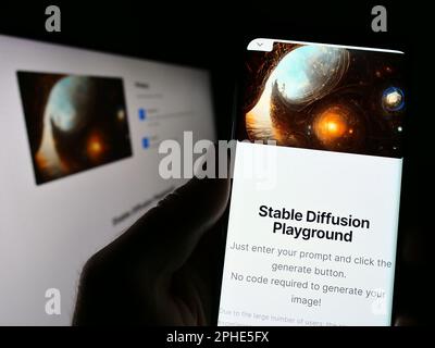 Person holding cellphone with web page and logo of deep learning model Stable Diffusion on screen. Focus on center of phone display. Stock Photo
