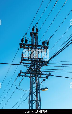 Old power utility and street light pole with cables and wires against blue sky in the evening Stock Photo