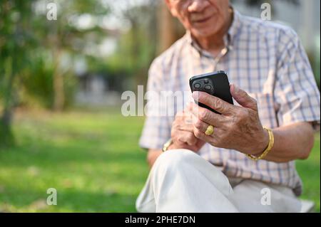 Close-up image of a happy Asian-aged retired man using his smartphone in the backyard. Stock Photo