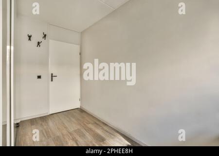 Interior design of hall with laminate floor and black hangers placed on white wall near entrance door Stock Photo