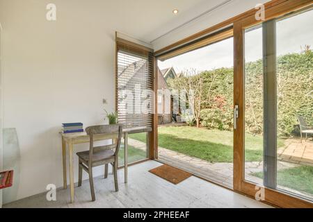 Wooden table with chair placed near open door to garden surrounded by green trees and plants Stock Photo