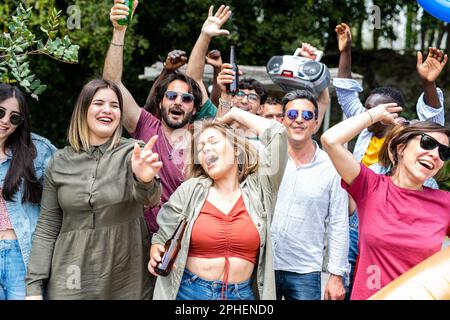 Big group of happy friends dancing and having fun at outside party, large mixed age range people celebrating holiday in a mansion, dancing and smiling Stock Photo