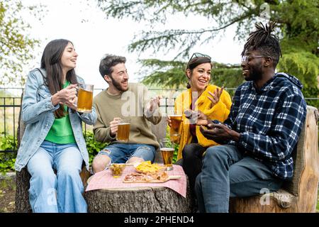 Friends drinking beer and eating snack outside at pub, diverse people having fun. Stock Photo