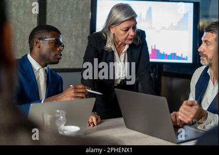 Thoughtful senior business woman concentrated on collaboration with colleagues during discussing new ideas for management project, multicultural partn Stock Photo