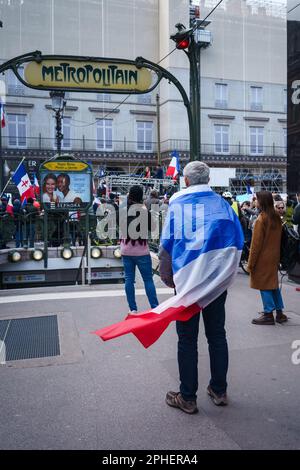 Paris, France. March 25, 2023. A man wearing a French flag in front of a metro entrance in a Protest against the pension reform outside the Palais-Roy Stock Photo
